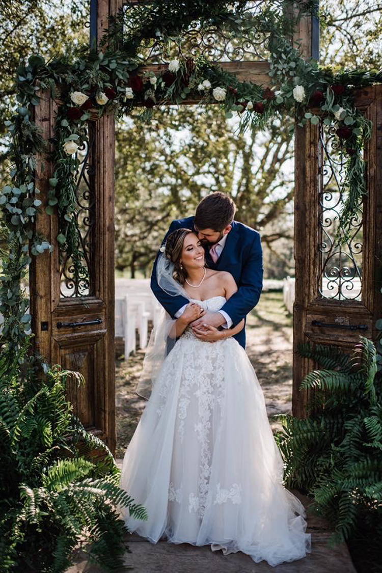 Bride & Groom in front of Wooden Door Wedding Ceremony Decor at The Venue at Southern Oaks | photo by MbM Photography | featured on I Do Y'all